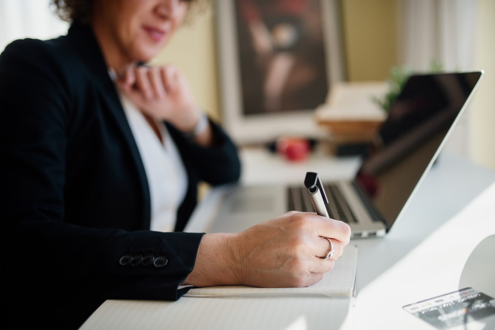 Professionnelle en veste sombre prenant des notes à côté d'un ordinateur portable — image d'illustration du support des cabinets partenaires